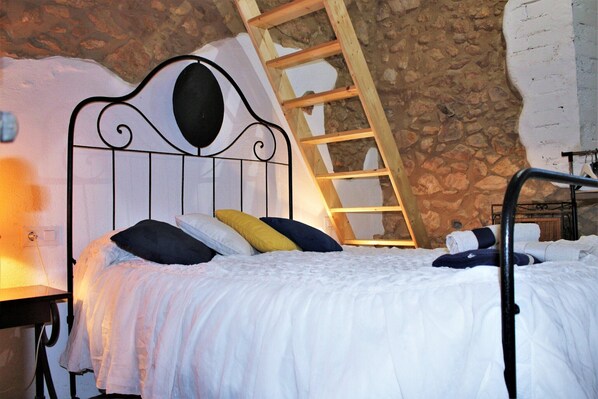 Een bed met een metalen hoofdbord, een houten ladder en een stenen muur.