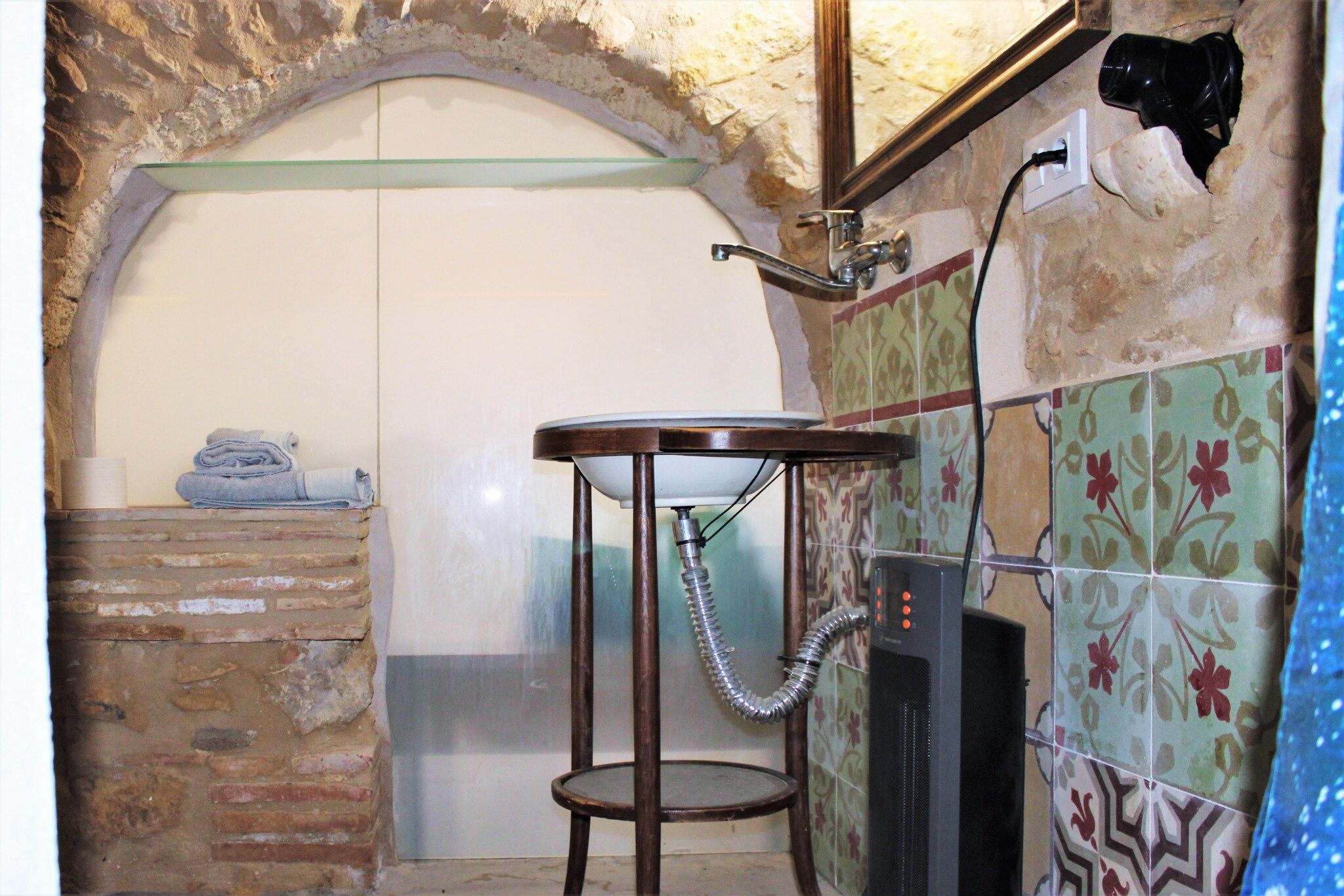 A bathroom with a stone wall, a small round table with a sink, and a towel stack.