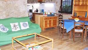 Ein gemütliches Wohnzimmer mit einem grünen Sofa, einem Holzkabinett, einem Esstisch mit Stühlen und einer Küche im Hintergrund.
