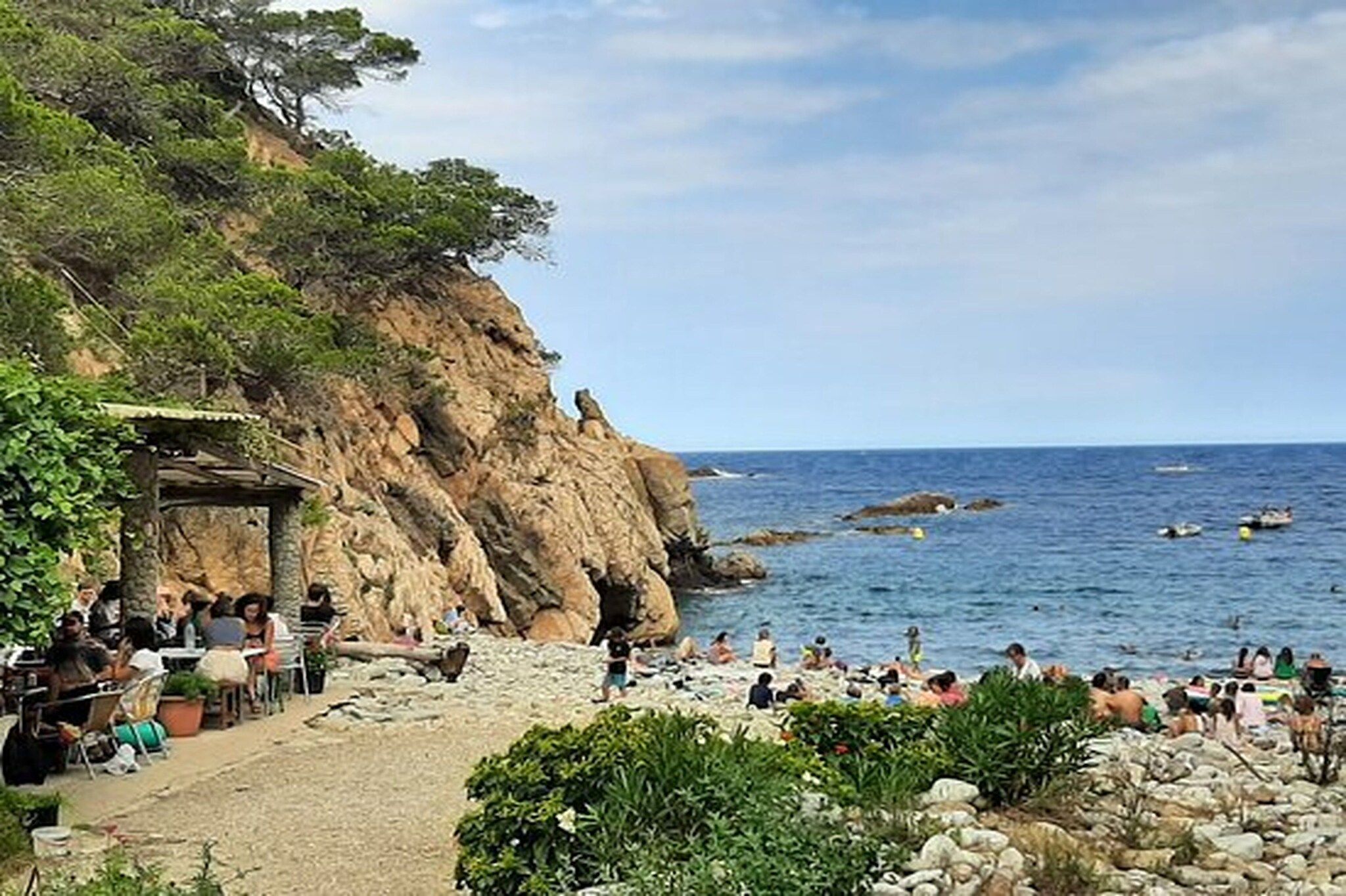A coastal area with a rocky cliff, a beach with people, and a sea view.