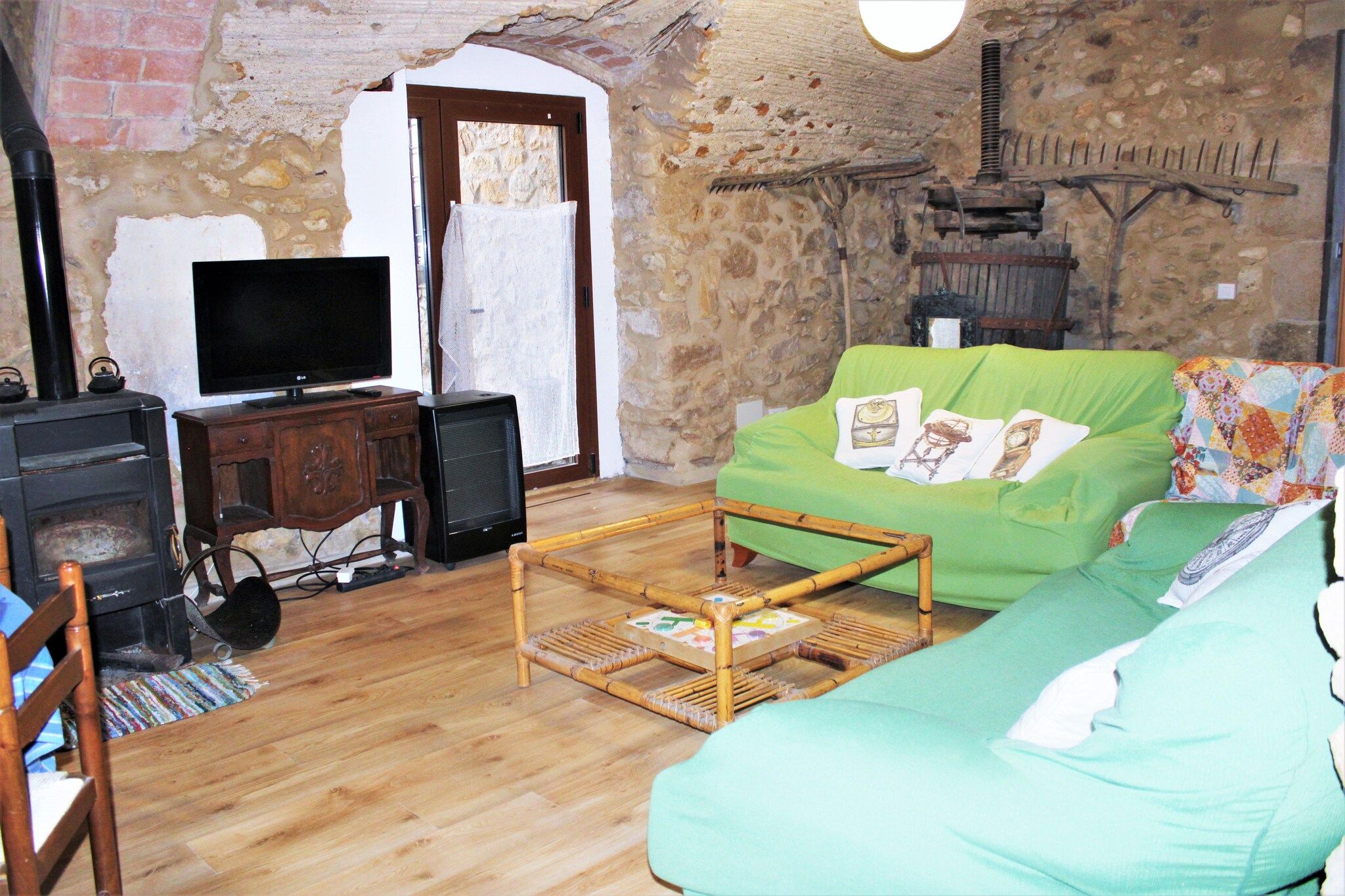 Una sala de estar rústica con una pared de piedra, un televisor, una mesa de madera y un sofá verde.