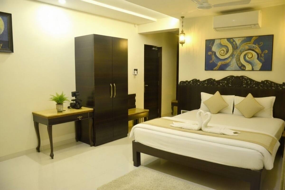 Quarto de hotel com cama grande, guarda-roupa, mesa de cabeceira com planta e um quadro na parede.