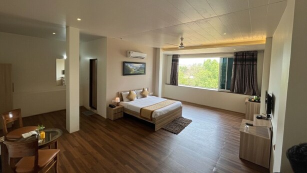 A modern hotel room with a large bed, a dining area, and a window with curtains.