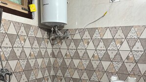 Ein Badezimmer mit Toilette, einem roten Eimer, einer Duschbrause und gemusterten Fliesen.