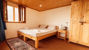 Ein Bett mit Holzbettgestell und weißen Leinentüchern, ein Nachttisch mit Wasserkocher und ein Kleiderschrank in einem Raum mit Holzbalken und einem Fenster.