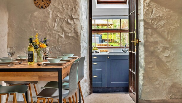 A dining area with a wooden table set for four, a vase with flowers, and a clock on the wall.