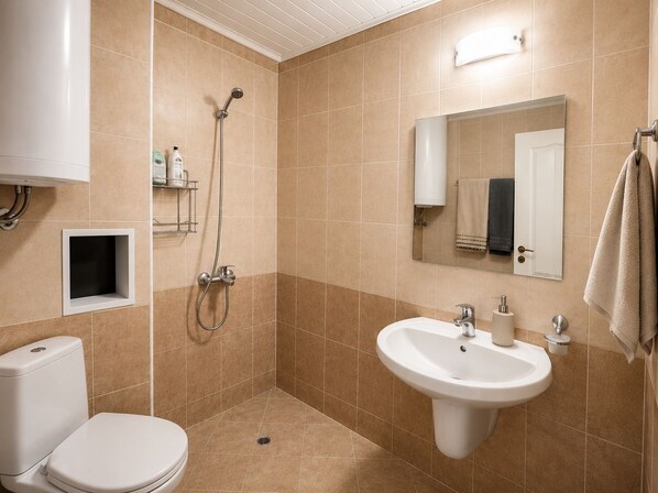 A bathroom with a toilet, sink, shower, and a mirror.