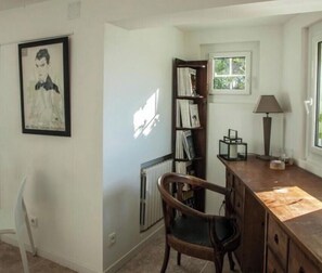 A room with a wooden desk, a chair, a bookshelf, a radiator, and a window with a view of trees.