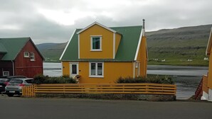 A yellow building with a green roof, a red barn, and a body of water in the background.