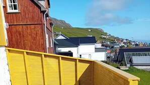 A wooden deck with a yellow fence, a metal chair, and a view of a town with houses and hills in the background.