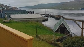 A coastal view with a wooden deck, a small shed, and a distant town across a body of water.
