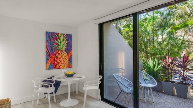 A modern dining area with a round table, white chairs, and a colorful pineapple artwork on the wall. - Sandy Cove Hideaway: Private, End-Unit, Walk to Village, Private Beach, Fishing Pier & Dog Friendly! (Siesta Key)
