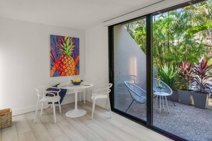 Un espace repas moderne avec une table ronde, des chaises blanches et une œuvre d’art colorée représentant un ananas, accrochée au mur.