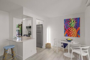 A modern kitchen with white cabinetry, a stainless steel refrigerator, and a dining area with white chairs and a table. - Sandy Cove Hideaway: Private, End-Unit, Walk to Village, Private Beach, Fishing Pier & Dog Friendly! (Siesta Key)