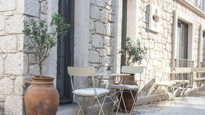 A row of outdoor tables and chairs with potted plants, set against a stone building facade. - Lupa Alacati (Cesme)