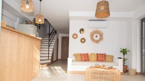 A modern living room with a staircase, a white sofa with patterned cushions, a wicker ottoman, and decorative wall art. - Lupa Alacati (Cesme)