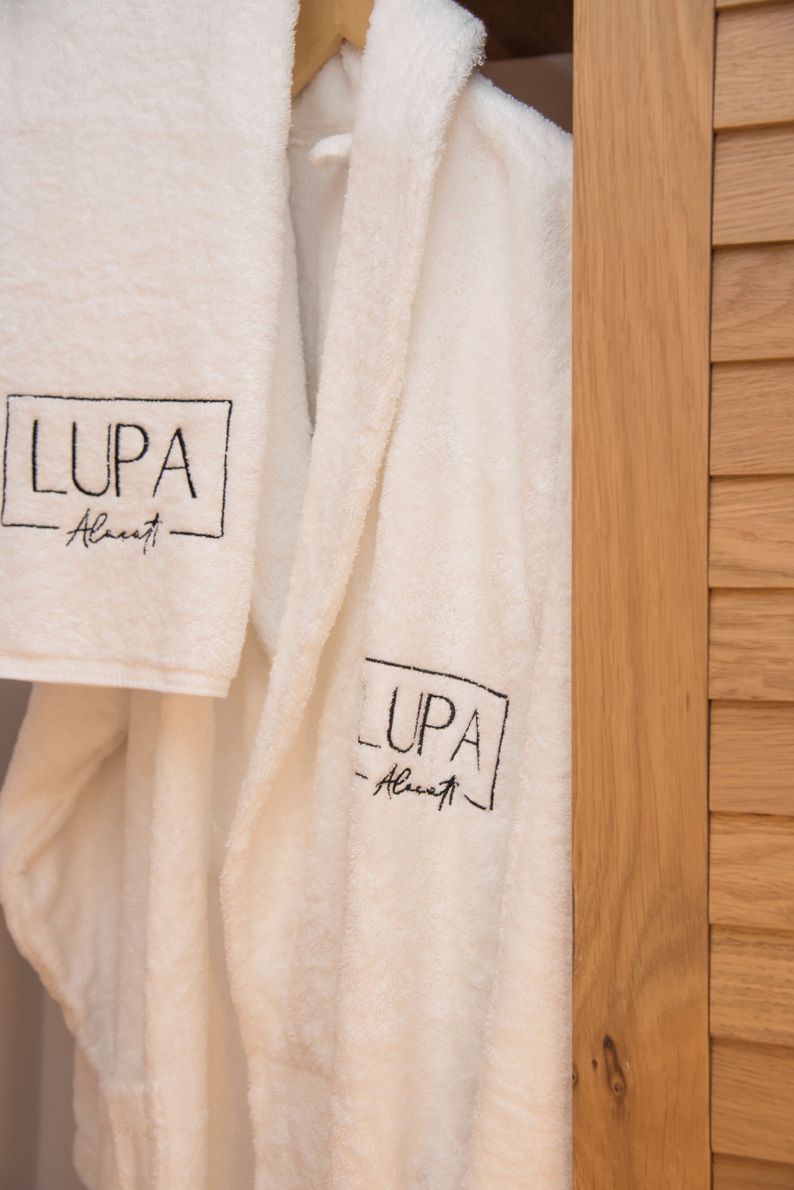 Two white bathrobes hanging on a wooden rack.