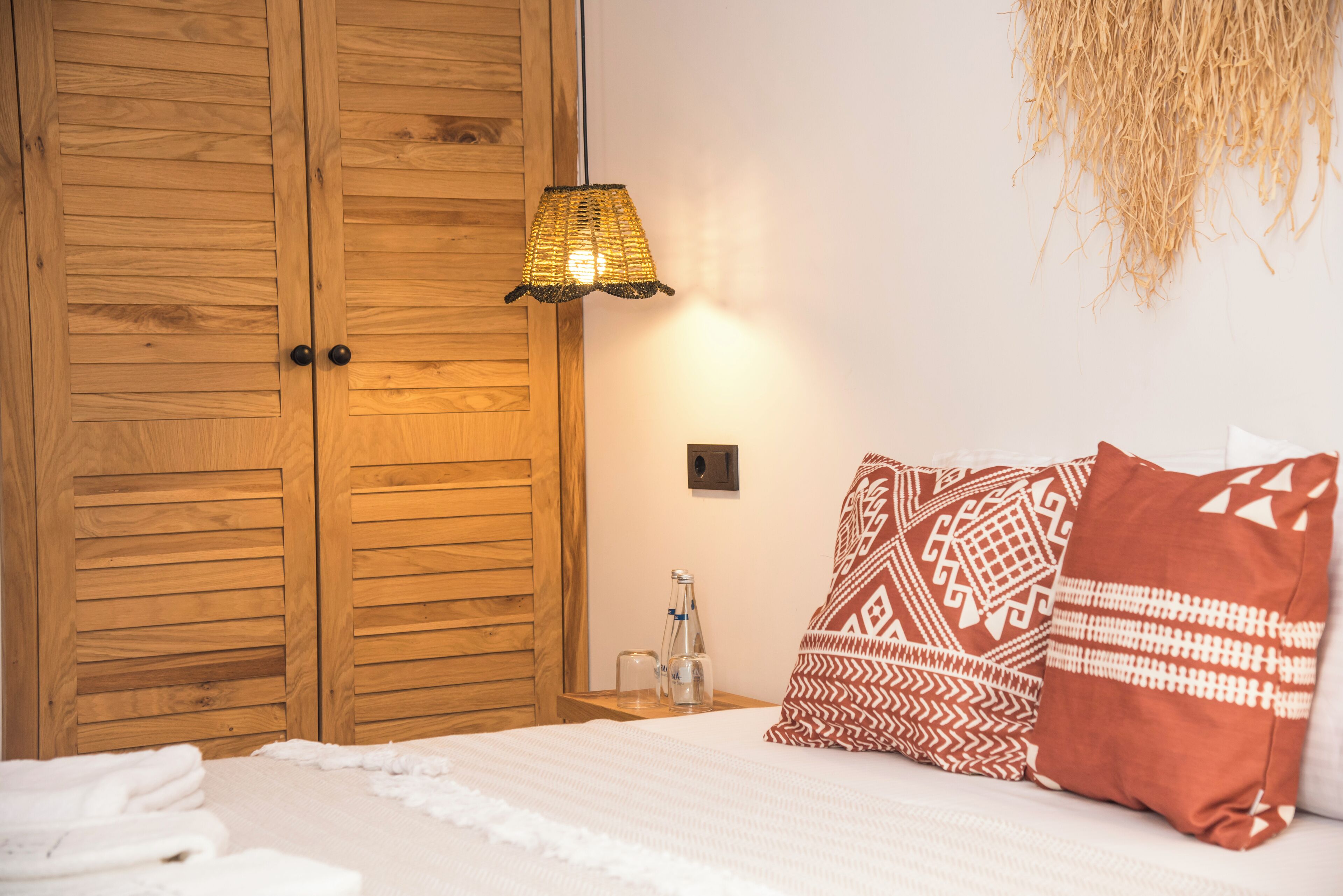 A bedroom with a bed, pillows, a nightstand, a lamp, and wooden wardrobes.