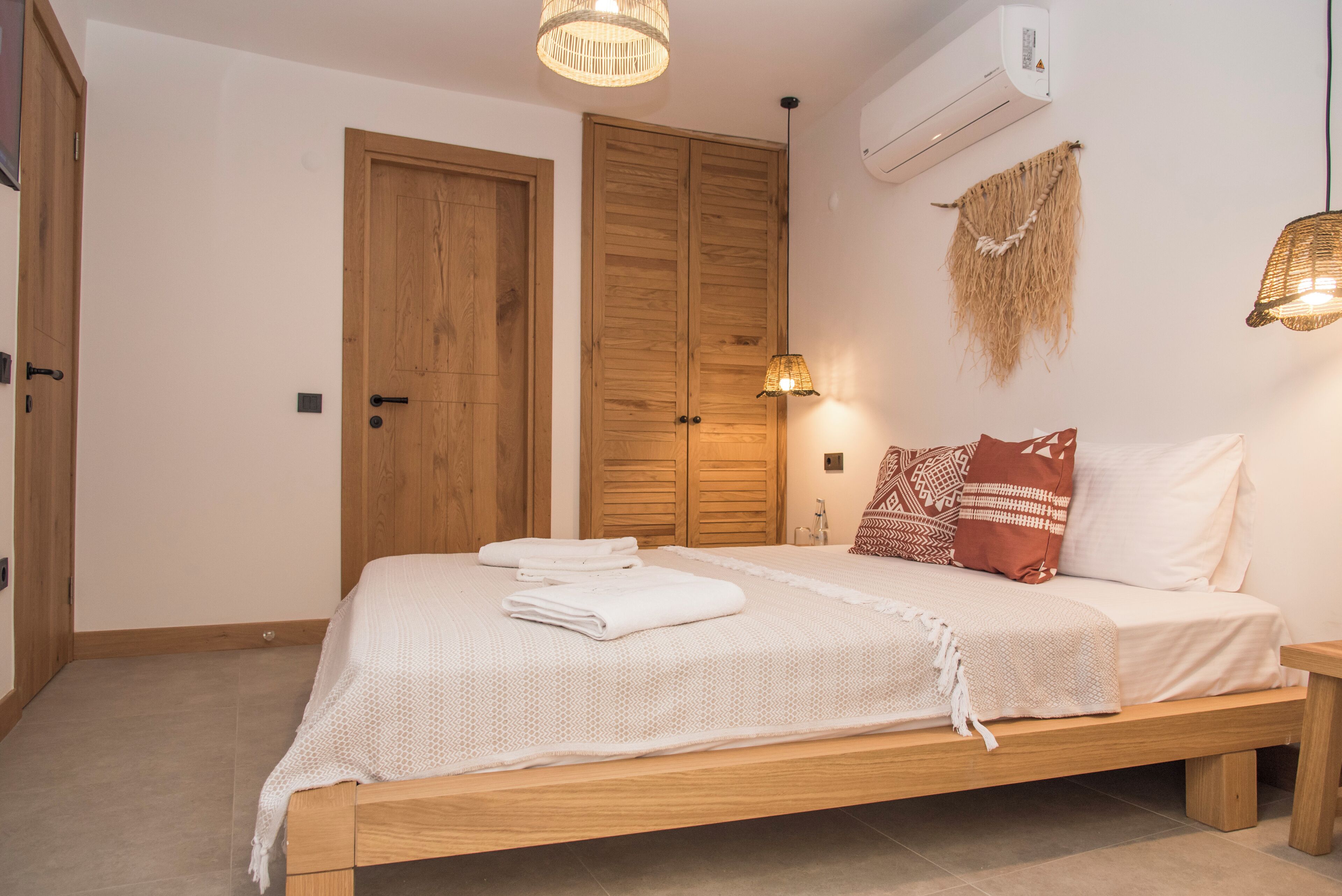 A bedroom with a wooden bed, white linens, a woven headboard, and a wall-mounted air conditioner.