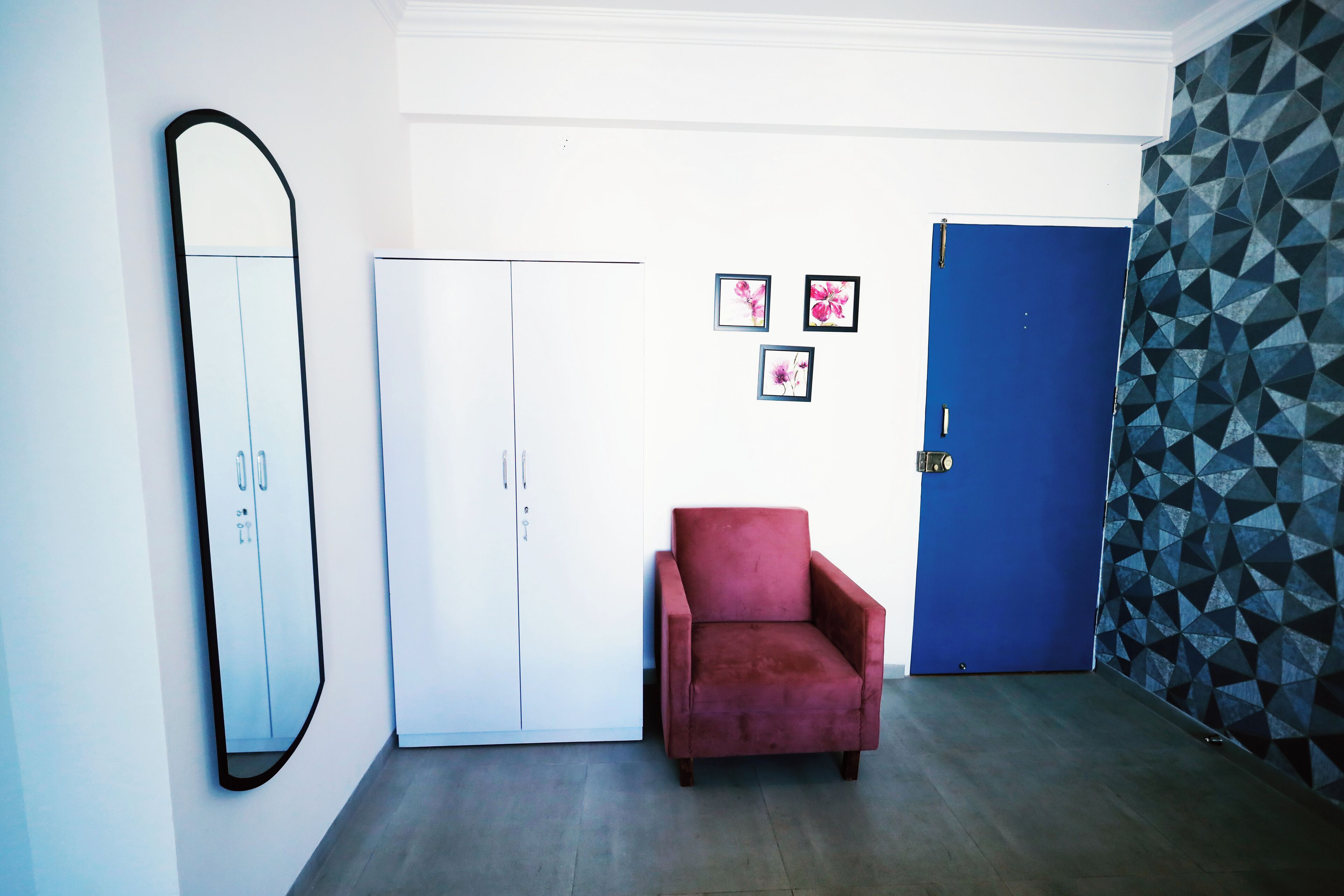 Una habitación con un armario blanco, un sillón rojo, una puerta azul y una pared con diseño geométrico.