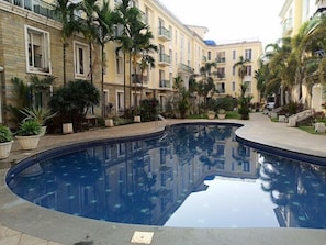 A swimming pool surrounded by multi-story buildings with balconies, palm trees, and potted plants. - Asta by Avim Hospitality (Arpora)