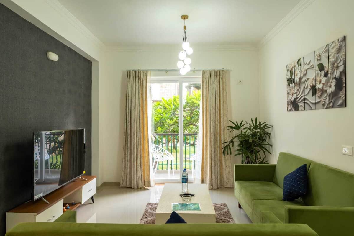 Un salon avec un canapé vert, un téléviseur à écran plat, une table basse et une grande fenêtre avec des rideaux.