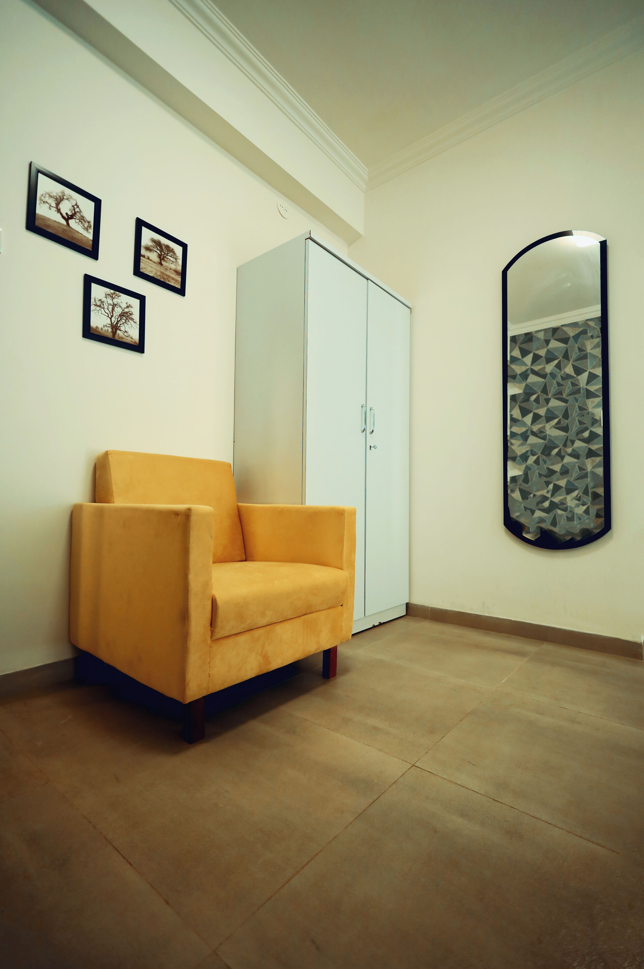 A room with a white wardrobe, a yellow armchair, and three framed pictures on the wall.
