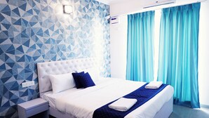 Ein modernes Schlafzimmer mit Wand in geometrischem Muster, einem weißen Bett mit blauen Akzenten, einem Deckenventilator und einem Fenster mit blauen Vorhängen.
