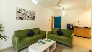 Ein Wohnzimmer mit zwei grünen Sofas, einem weißen Couchtisch, einem Deckenventilator und einer Küchenzeile mit Holzschränken.