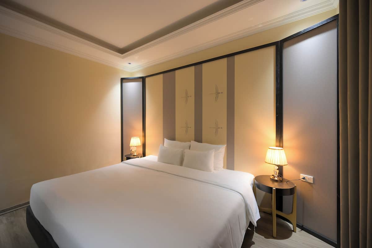 A neatly made bed with white linens, a bedside table with a lamp, and a wall with decorative panels.