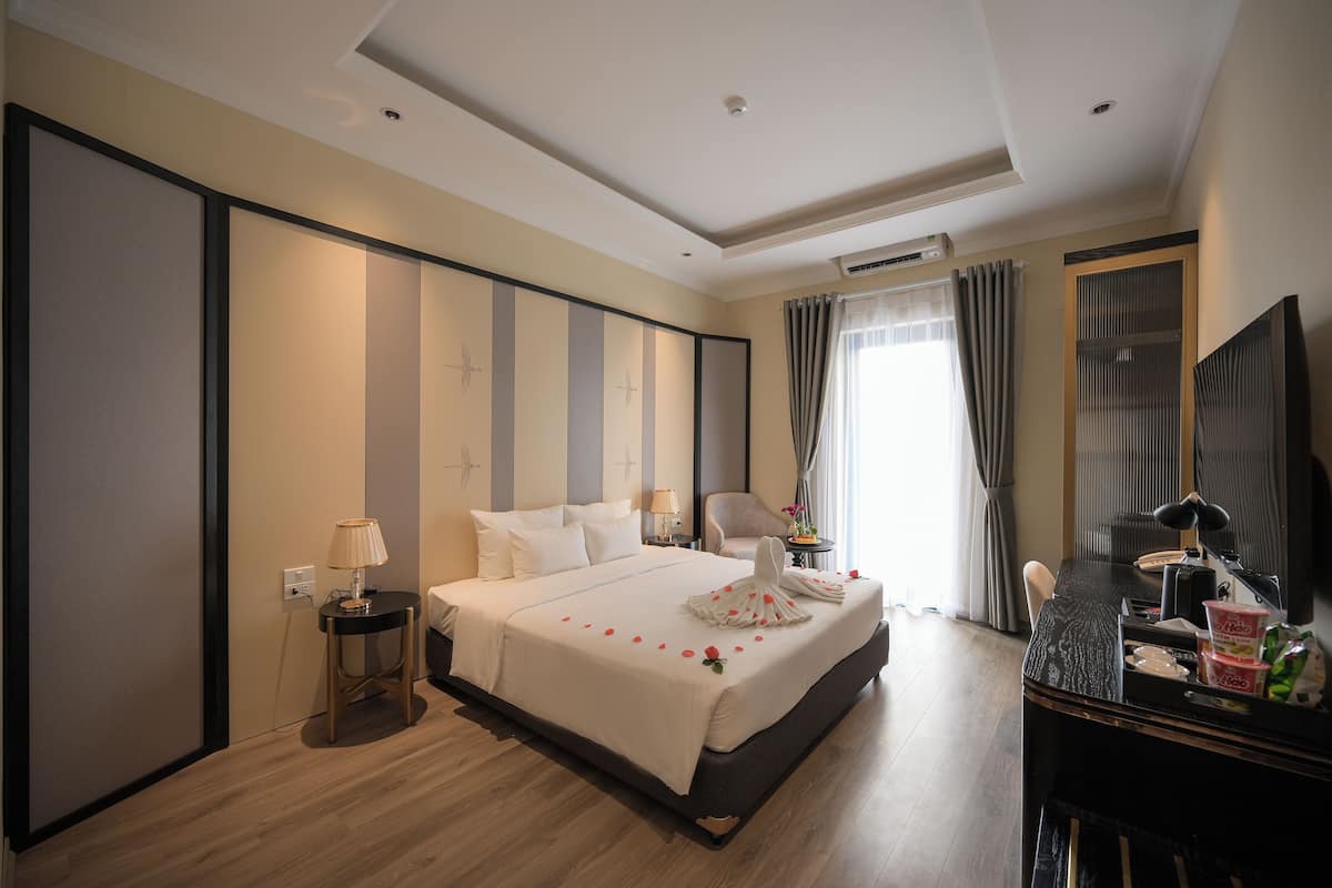 A hotel room with a large bed, a desk with a computer, a chair, and a TV.