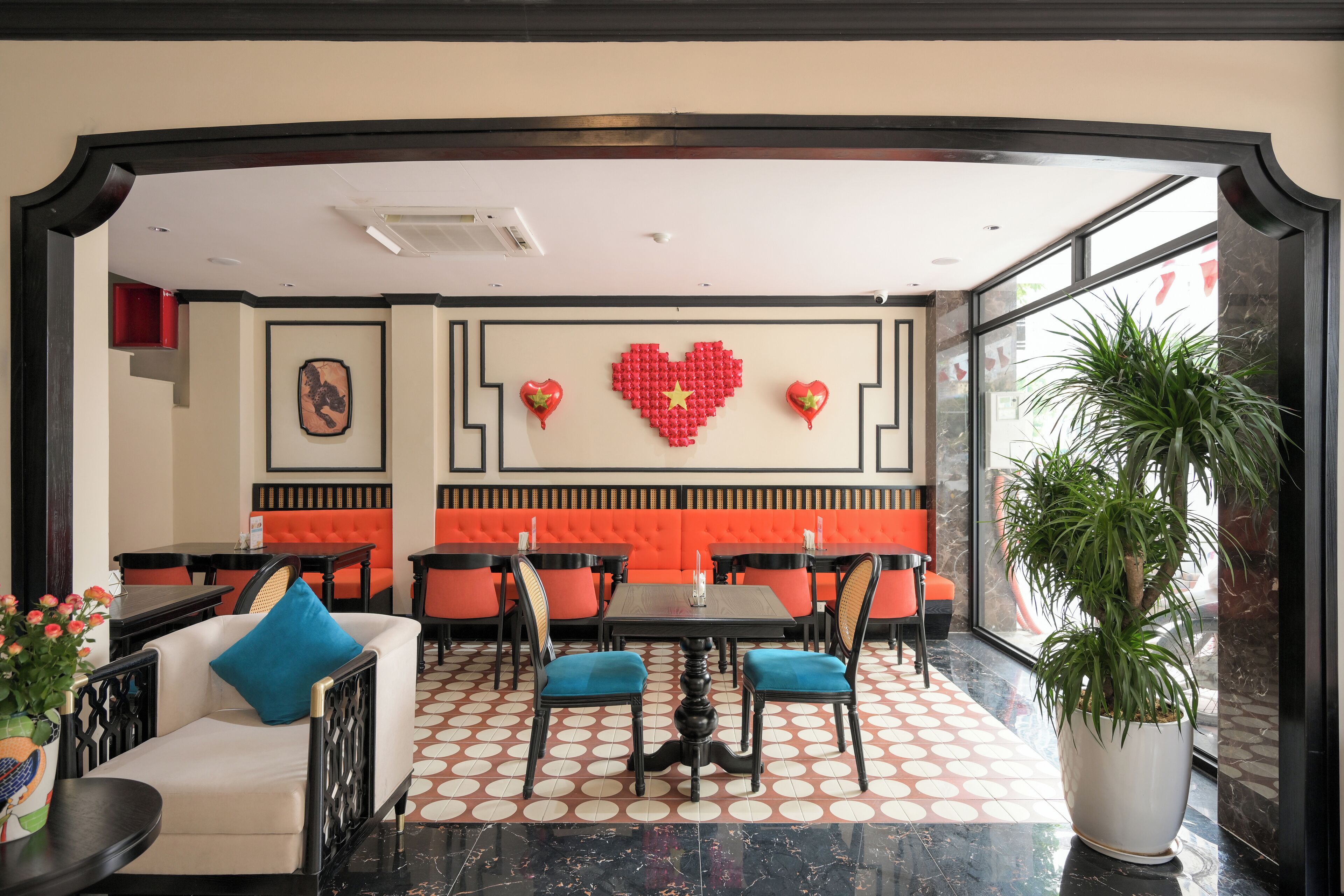 Een restaurant met een hartvormige wanddecoratie, oranje gestoffeerde zitplaatsen en een potplant.