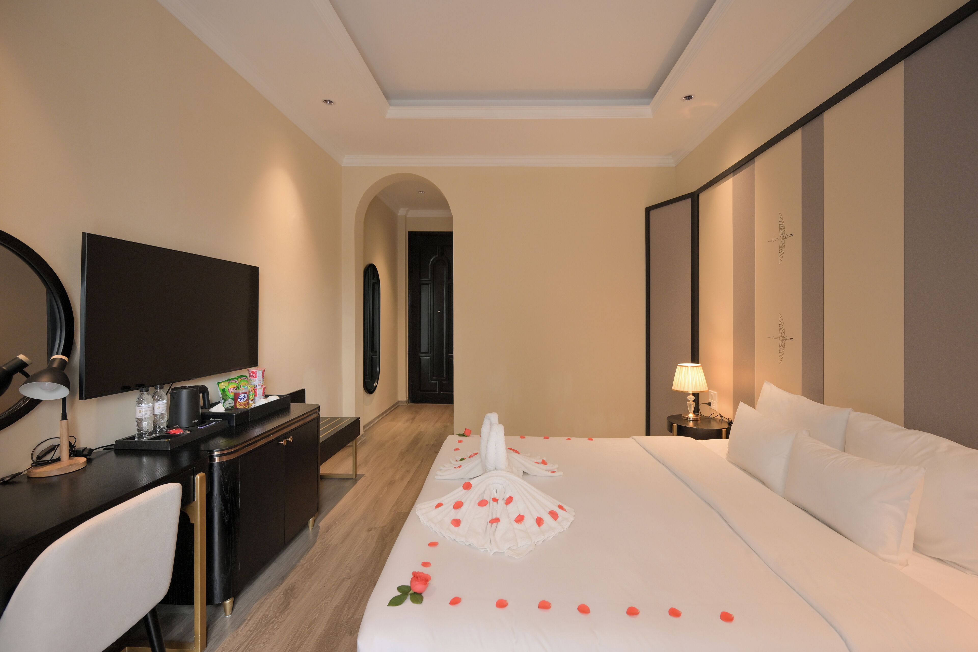 A hotel room with a bed, a desk, a TV, and a door leading to another room.