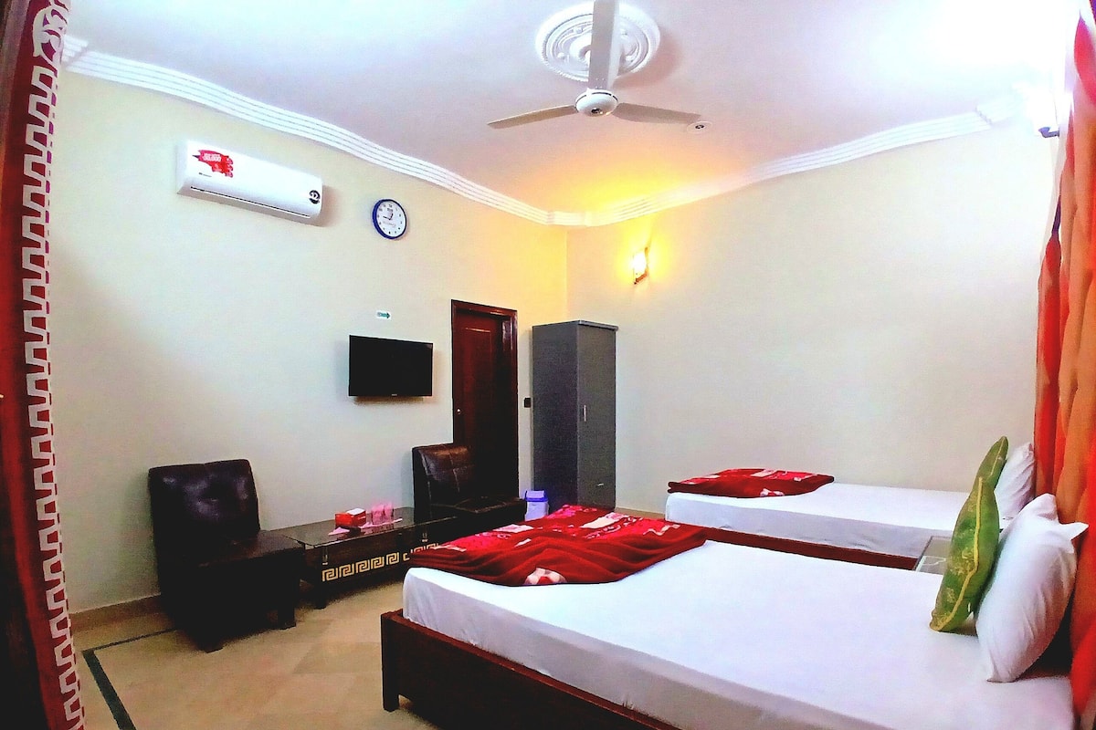 A hotel room with two beds, a TV, an air conditioning unit, and a ceiling fan.