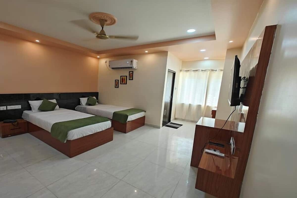 A hotel room with two beds, a ceiling fan, an air conditioning unit, a wooden desk, and a television.
