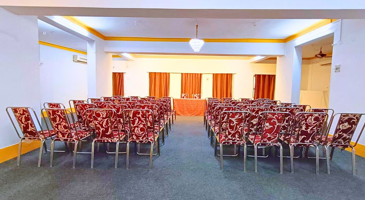 Un salón de conferencias con filas de sillas, un escenario con cortinas y un candelabro.