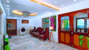 A lobby with a sofa, a wall-mounted air conditioner, a chandelier, and a wooden door with a window. - Hotel Vijay Deluxe (Sultanpur)