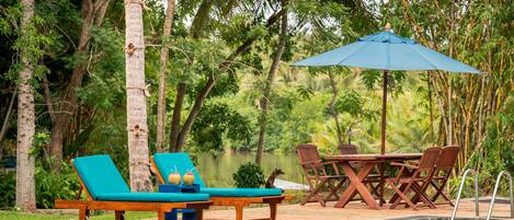 Zona junto a la piscina con sillones, una mesa y una sombrilla.