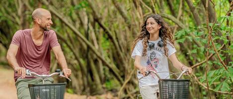 Two people riding bicycles on a dirt path surrounded by trees.
