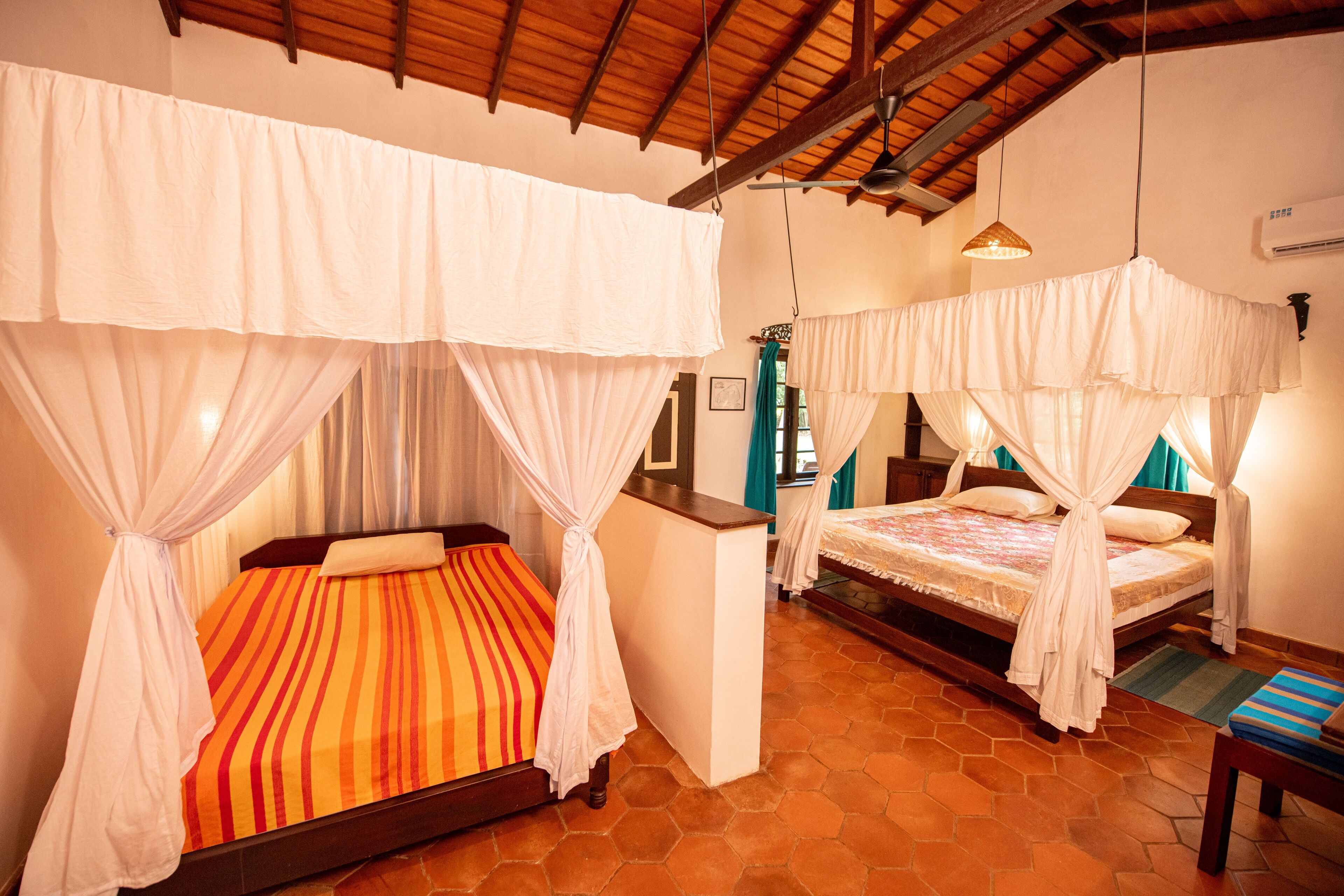 A hotel room with two beds, each with a canopy. The room has a tiled floor and a wooden ceiling.