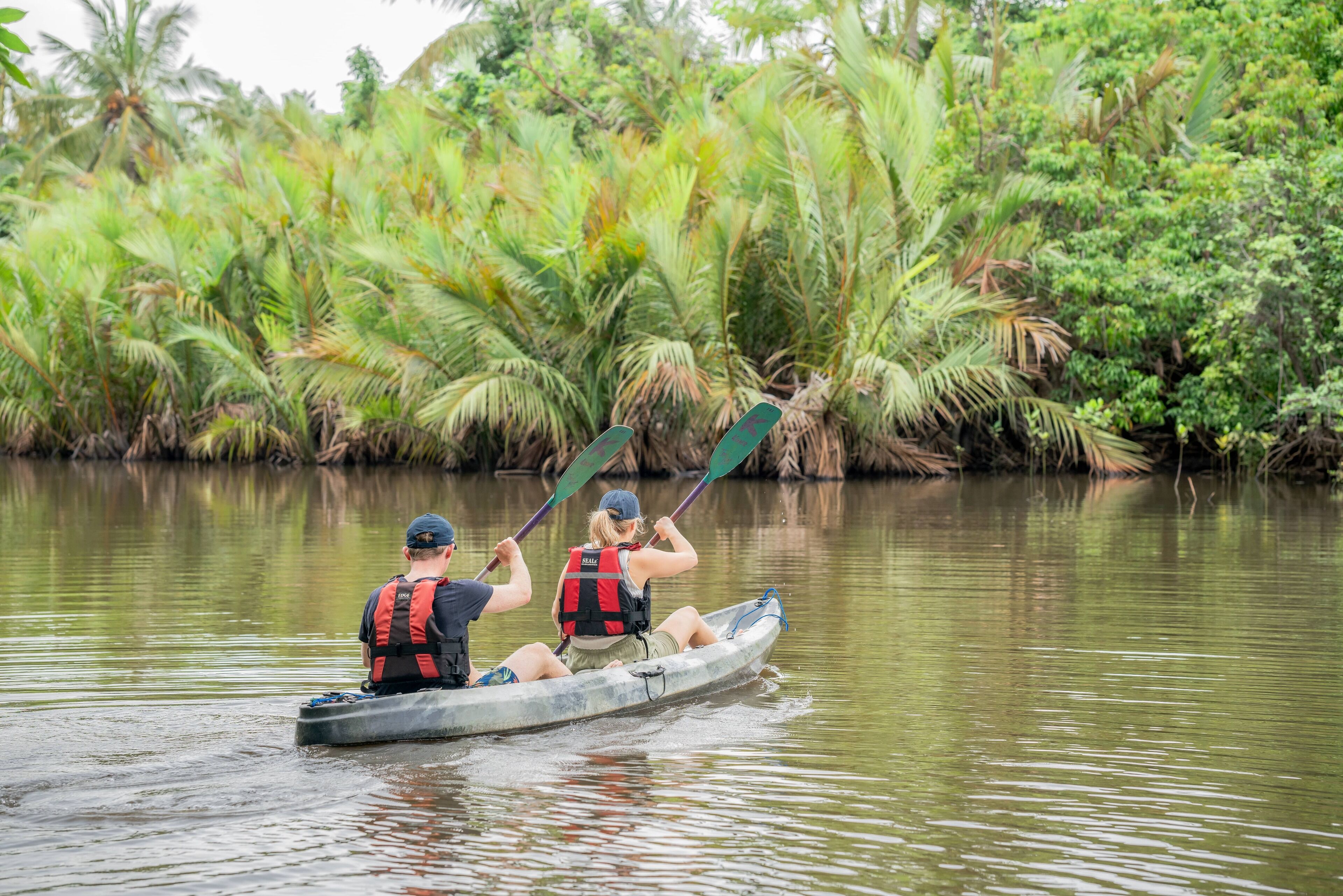 Two people in a canoe on a calm river surrounded by lush greenery.