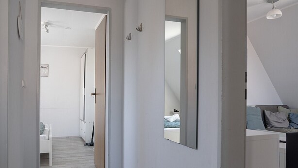 Un pasillo con piso de madera, un espejo grande y una cama con almohadas al fondo.