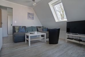 A modern living room with a sofa, a coffee table, a TV on a stand, and a window.