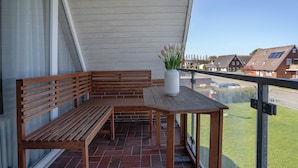 Un balcón con un banco y una mesa de madera, una planta en maceta y vistas a casas.