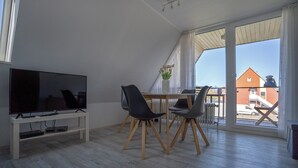 Una sala de estar moderna con televisor, mesa de comedor, sillas y vistas al exterior.