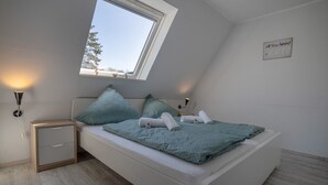 Un dormitorio con tragaluz, cama con colcha color turquesa, dos lámparas de noche y una mesita de noche pequeña.
