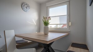 Moderni huone, jossa on puinen pöytä, valkoiset tuolit, kello ja ikkuna, jossa on sälekaihtimet.