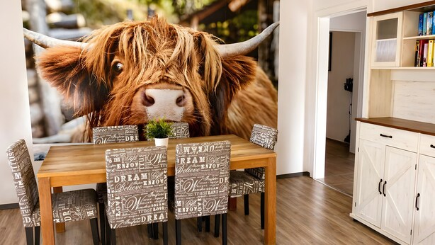 Ein Essbereich mit einem Holztisch, gemusterten Stühlen und einem großen Wandgemälde mit Stier-Motiv.