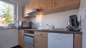 Moderni keittiö, jossa on puiset kaapit, mikroaaltouuni, kahvinkeitin ja astianpesukone.