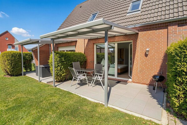 A house with a covered patio, a table with chairs, and a barbecue grill.